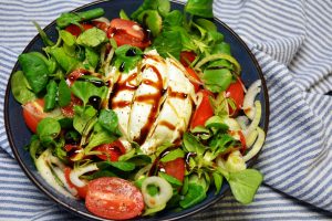 Burrata Salat mit halbierten Kirschtomaten in mehreren Farben, Babyspinat, roten Zwiebeln und Balsamico-Creme auf einer Platte