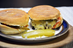 Zwei selbst gemachte Cheeseburger mit Grillstreifen im Brötchen, geschmolzenem Käse und Gewürzgurke auf einem Teller