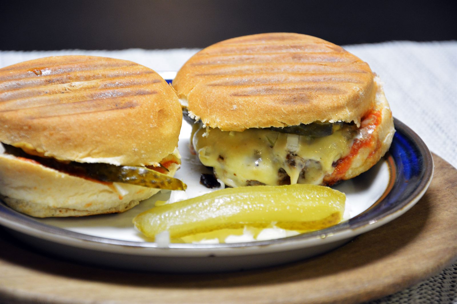 Zwei selbst gemachte Cheeseburger mit Grillstreifen im Brötchen, geschmolzenem Käse und Gewürzgurke auf einem Teller