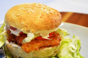 Crispy Chicken Burger mit knusprig paniertem Hähnchen, Tomate, Salat und Chili-Mayo in einem Sesambrötchen