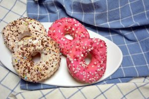 Selbst gemachte Donuts mit rosa und weißem Zuckerguss und buntem Streusel auf einer Platte