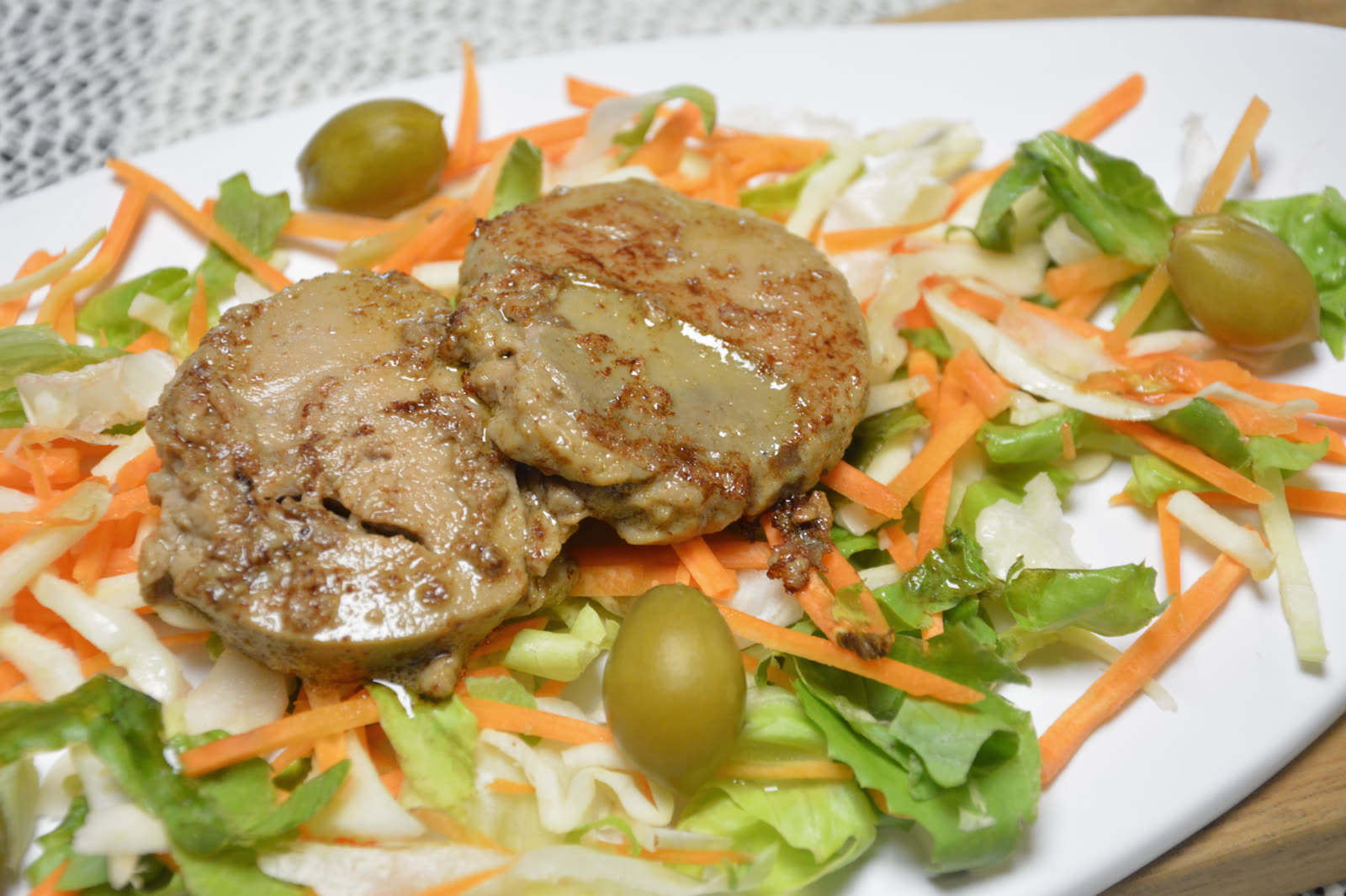 Gebratene Foie Gras in zwei runden Scheiben auf einem Bett aus Salat mit Karotte, Weißkohl und grünen Babypfirsichen