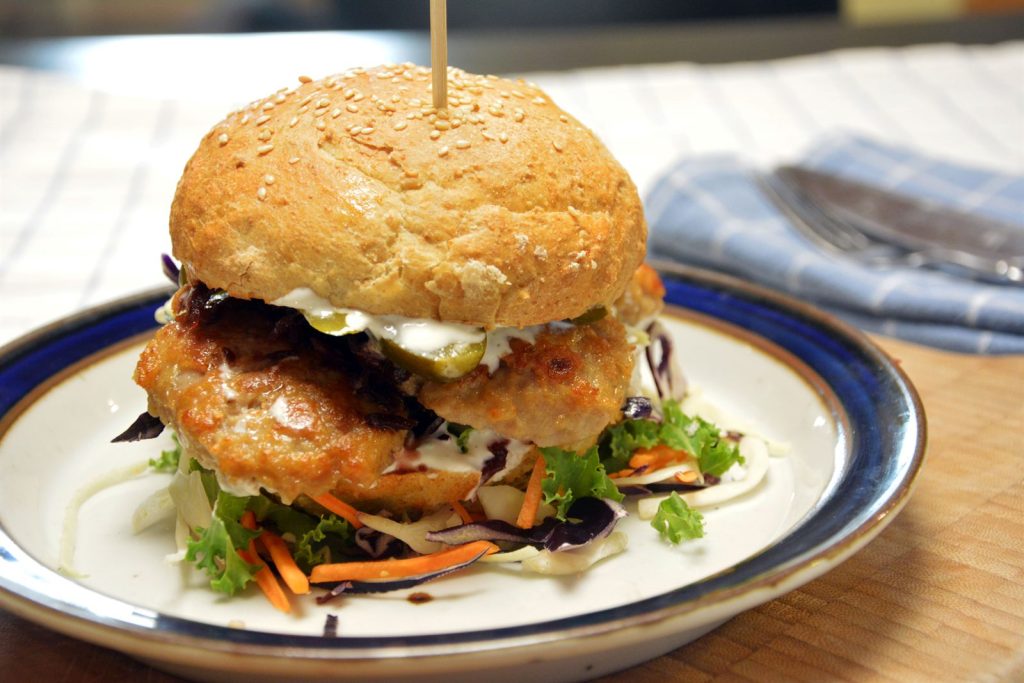 Frikadellenbrötchen mit Krautsalat, Rotkohl und Gewürzgurkenscheiben, zusammengehalten von einem Holzspieß