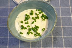 Kräuterdip mit Schnittlauch in einer türkisfarbenen Schale auf einem blau karierten Geschirrtuch