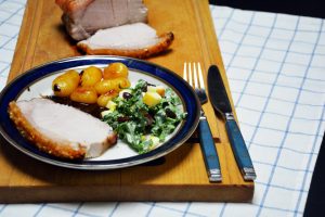 Krustenbraten sous vide in Scheiben geschnitten mit knuspriger Kruste, dazu karamellisierte Kartoffeln, Bratensoße und Grünkohlsalat