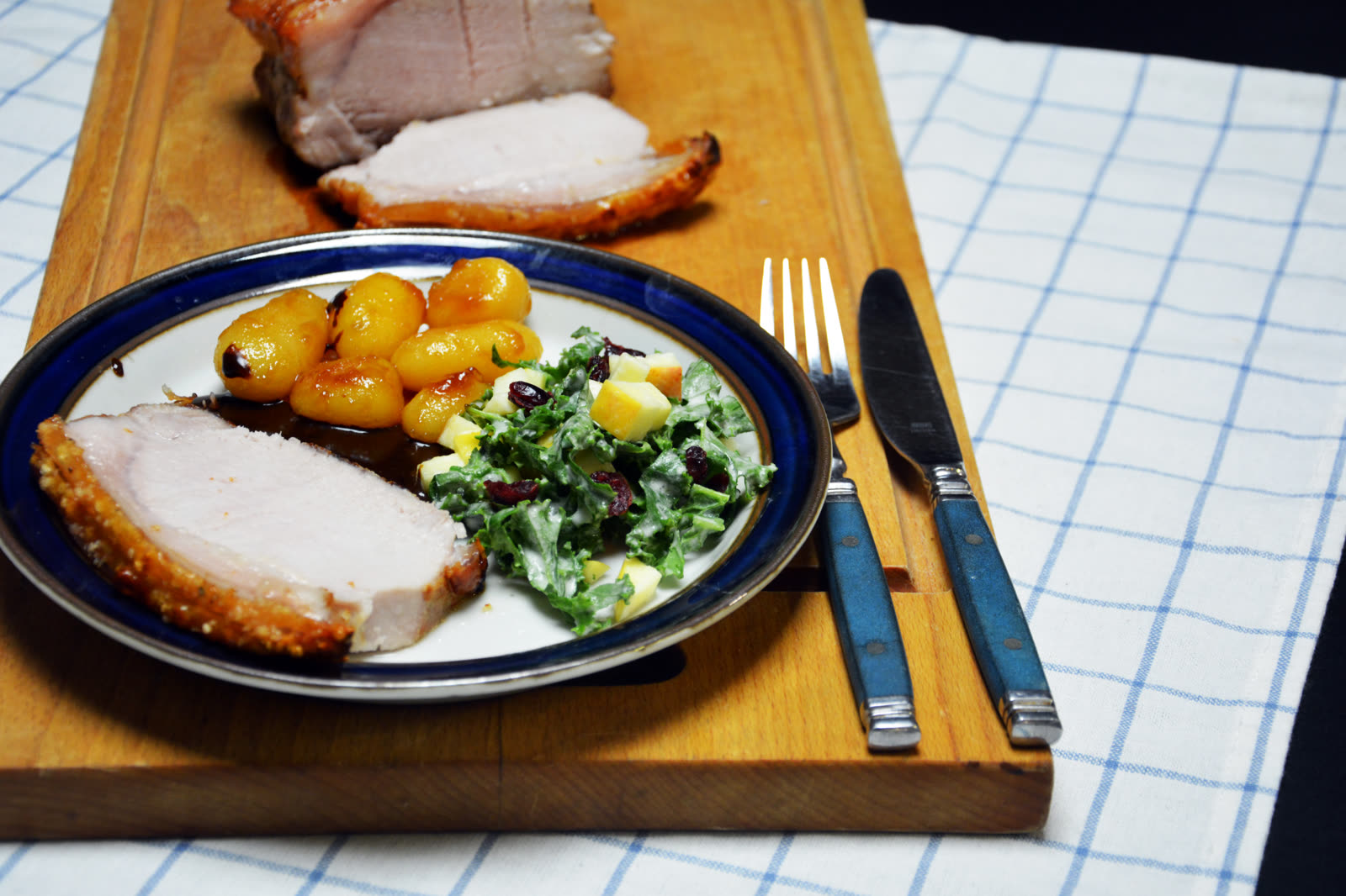 Krustenbraten sous vide in Scheiben geschnitten mit knuspriger Kruste, dazu karamellisierte Kartoffeln, Bratensoße und Grünkohlsalat