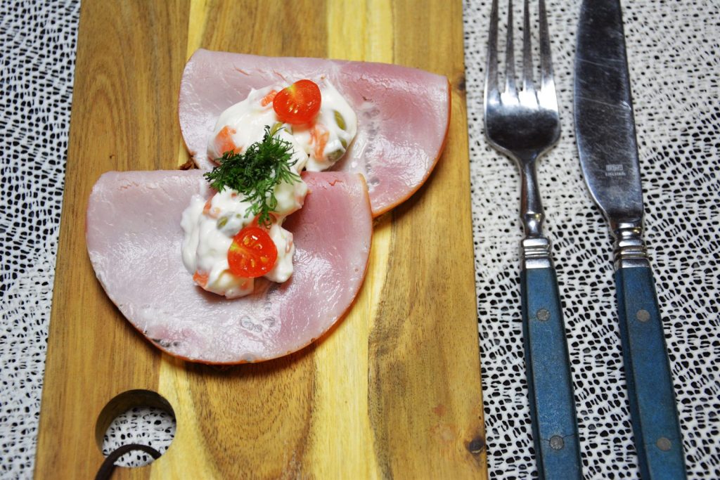 Erbsen-Möhren-Salat mit Spargel auf einer gefalteten Scheibe Kochschinken auf Vollkornbrot, garniert mit einer halbierten Kirschtomate und Dill