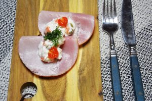 Erbsen-Möhren-Salat mit Spargel auf einer gefalteten Scheibe Kochschinken auf Vollkornbrot, garniert mit einer halbierten Kirschtomate und Dill