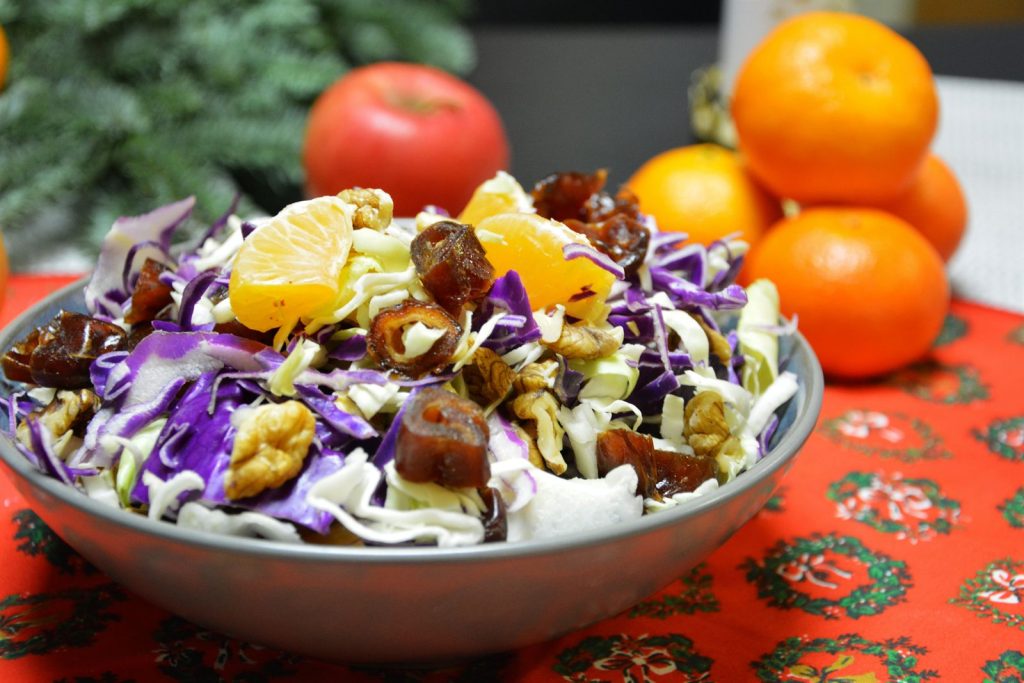 Weihnachtssalat aus geschnittenem Chicorée und Rotkohl mit Datteln, Walnüssen und Clementinenspalten in einer Metallschüssel auf einer roten weihnachtlichen Tischdecke